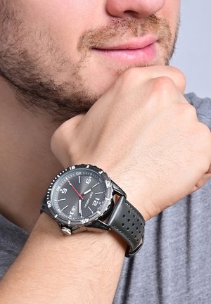 Analoge Armbanduhr mit schwarzem rundem Zifferblatt, silbernen Akzenten, rotem Sekundenzeiger und einem perforierten dunkelgrauen Silikonarmband.