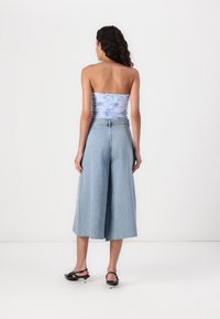 Jasnoniebieskie dżinsowe kuloty o szerokich nogawkach, zestawione z topem bez ramiączek w kwiatowy wzór. Stylowe czarne klapki na obcasie uzupełniają całość.