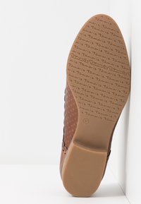 Chaussure marron à petit talon avec une surface texturée. La semelle en caoutchouc présente un logo de marque en relief, taille 37, et des bords lisses.