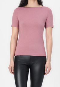 Krátký rukáv v barvě zaprášené růžové, vyrobený z měkkého materiálu. Má kulatý výstřih a přiléhavý střih, doplněný lesklými černými legínami.