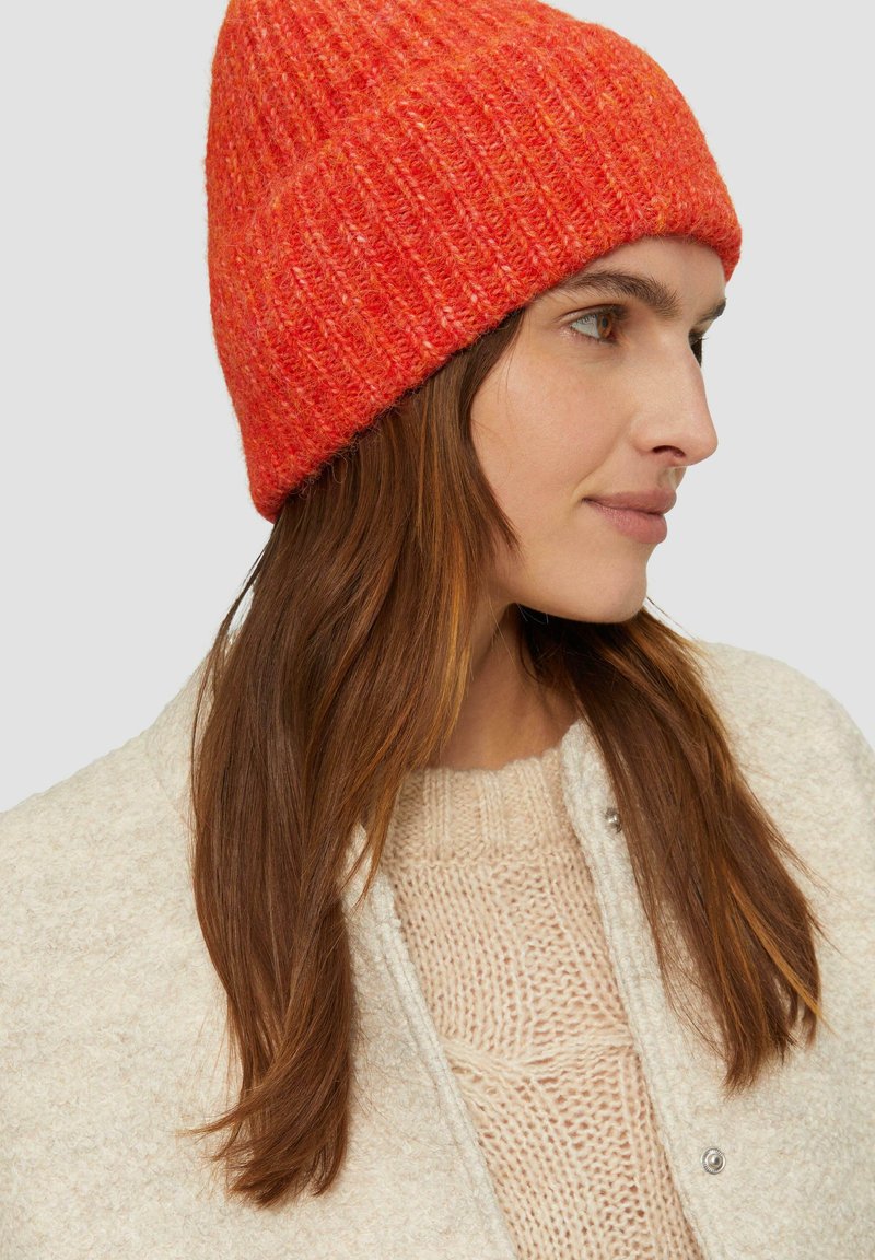 Rote Strickmütze mit gerippter Textur und umgeschlagenem Bund. Weiches Material mit unterschiedlichen Orangetönen und subtilen Sprenkeln.