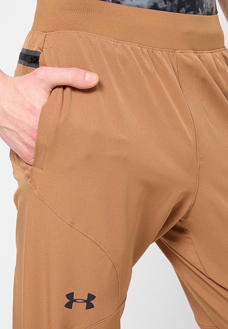 Pantalones deportivos marrones hechos de un tejido ligero que cuentan con una cintura elástica, un bolsillo lateral con cremallera negra y un detalle de logo en la pierna izquierda.