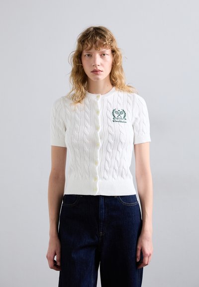 Cardigan blanc à manches courtes avec un motif en mailles torsadées, forme ajustée et encolure ronde. Présente des boutons jaunes et des détails brodés verts.