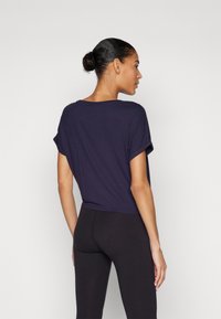 Marineblå t-skjorte med korte ermer og rullede mansjetter, løs passform og myk tekstur, kombinert med svarte leggings. Ingen synlige logoer eller mønstre.