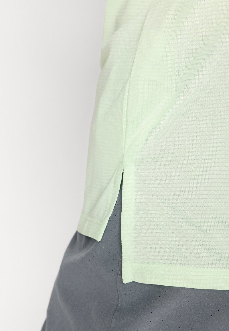 T-shirt de sport texturé vert clair avec des fentes sur les côtés, assorti à un short gris avec de petites perforations.