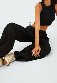 Pantalones negros de pierna ancha hechos de tela suave, con un cordón en la cintura. Combinados con un top corto negro y zapatillas de color claro.