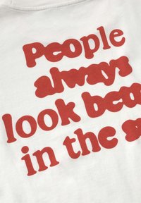 Weißer Stoff mit rotem, fett gedrucktem Text "People always look bad in the summer" in einer verspielten, abgerundeten Schriftart.