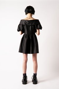 Fekete, váll nélkül viselhető ruha puffos ujjal, redőzött derékkal és bővülő szoknyával. Fekete harci csizmával és bokazoknival párosítva.