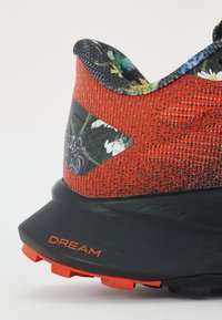 Bottine de sport rouge avec un dessus texturé, des accents à motif floral, un talon noir et une étiquette "DREAM" orange bien visible sur la semelle.