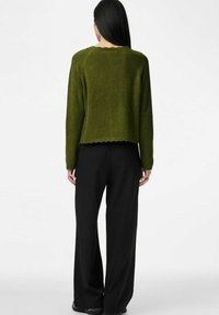 Zaļš adīts džemperis ar viļņotu apakšmalu, kombinēts ar melnām svārku bikšu biksēm ar šaurām svītrām. Audums šķiet mīksts un ar tekstūru.