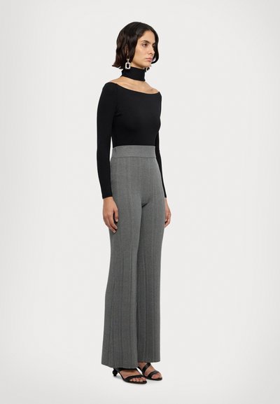 Sort langærmet top med off-shoulder design, parret med grå ribbede vide bukser og sorte stroppede sandaler.
