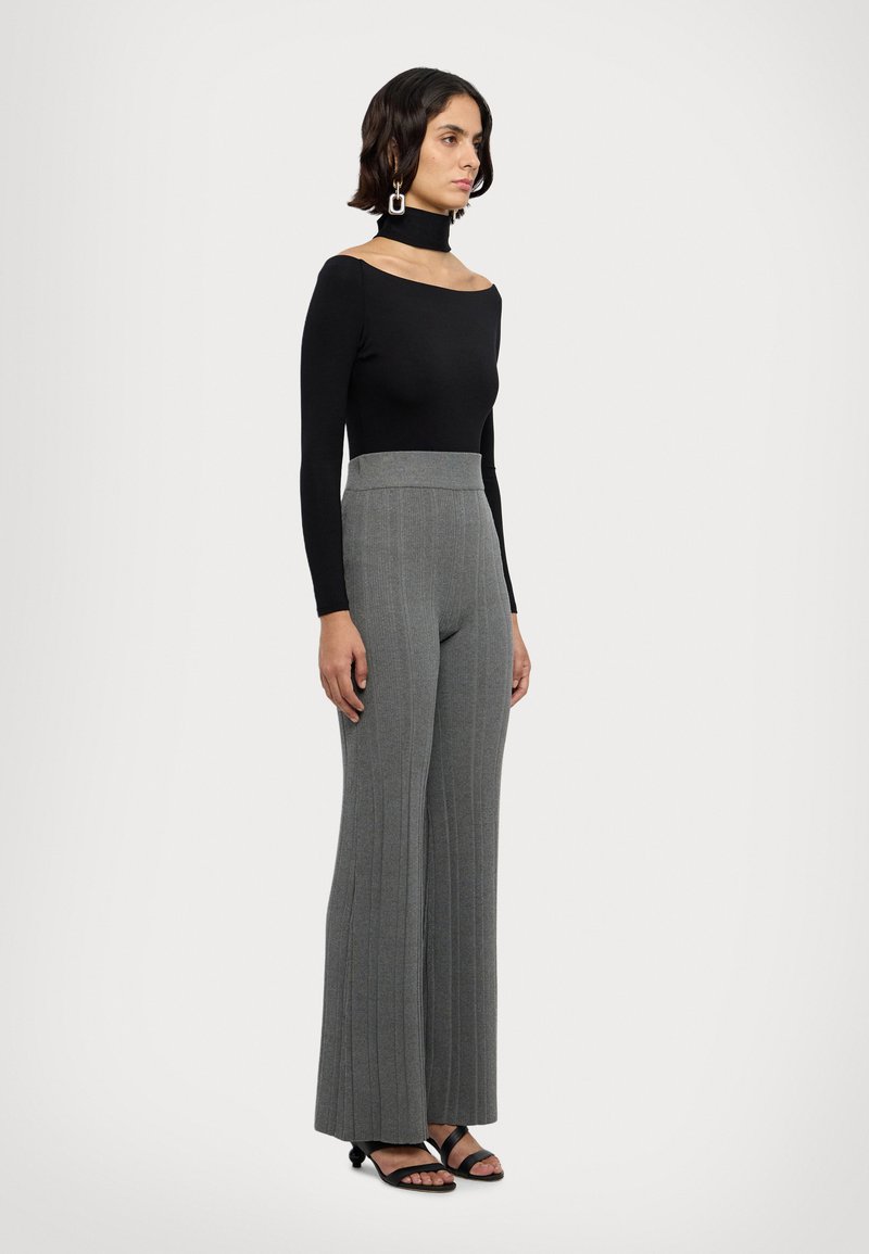 Bluză neagră cu mâneci lungi, design off-shoulder, asortată cu pantaloni evazați gri cu dungi și sandale negre cu barete.