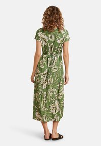 Groene maxi-jurk met korte mouwen, met een bloemenpatroon in wit en beige. Vastgebonden in de taille, zachte textuur en vloeiende uitstraling.