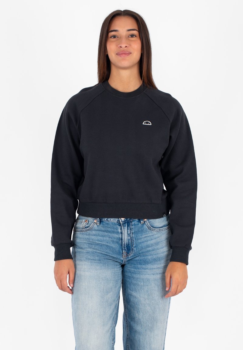 Felpa nera corta con maniche raglan, polsini a costine e un piccolo logo bianco sul petto. Abbinata a jeans di denim azzurro chiaro.