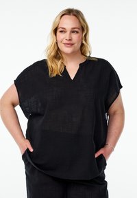Mustat, lyhythihaiset puserot, joissa on V-kaula-aukko ja teksturoitu kangas. Reilu istuvuus, epätasainen helma, kädet taskuissa, minimaalinen yksityiskohtaisuus.