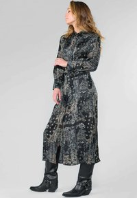 Zwarte jurk met paisleypatroon, lange mouwen met knopen, getailleerde taille en een lengte tot de knie. Draag het met zwarte laarzen tot de knie.