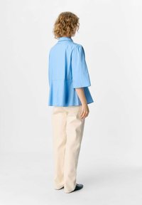Lichtblauw kortearm top met een peplum ontwerp, kraag en zachte textuur; gecombineerd met crème kleurige wijde broekspijpen en zwarte schoenen.