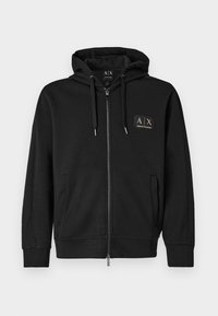 Crna zip-up dukserica s prednjim džepovima, kapuljača s ušicama za zatezanje i mala zlatna Armani Exchange oznaka na lijevoj strani prsnog koša.