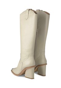 Botas altas hasta la rodilla hechas de suave cuero beige con punta afilada, tacón grueso, cremallera lateral y tirador decorativo en la parte superior.