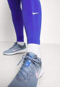 Leggings sportivi blu con logo Nike bianco, abbinati a scarpe Nike grigie e rosa con superiore in rete testurizzata e suole bianche.