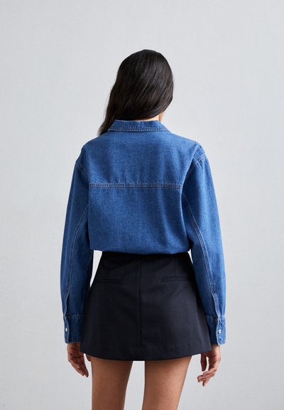 Blå denimskjorte med krage, lange ermer og knappeoppstrenginger. Kombinert med et svart mini skjørt. Enkelt design, uformell stil.