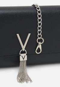 Black textured leather bag with silver chain strap, featuring a large "V" emblem and a tassel detail hanging from a silver clasp.