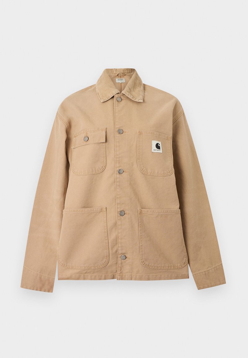 Beige overhemdjack met vier zakken aan de voorkant, waarvan één zak een zwart-witte Carhartt-logo patch heeft.