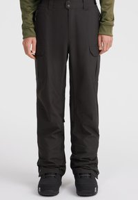 Sorte vandtætte bukser med lynlåslommer, elastisk talje og forstærkede manchetter, parret med sorte sneboots.