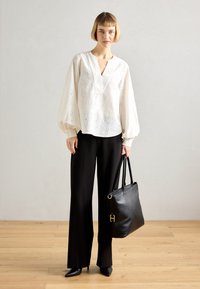 Blusa bianca con ricamo a occhio, scollatura a V profonda e maniche a sbuffo; abbinata a pantaloni neri a gamba larga e una borsa a tracolla in pelle nera.