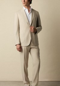 Beige pak met een gestructureerde blazer en rechte broekspijpen, gecombineerd met een wit overhemd met knopen, met een schone, op maat gemaakte uitstraling.
