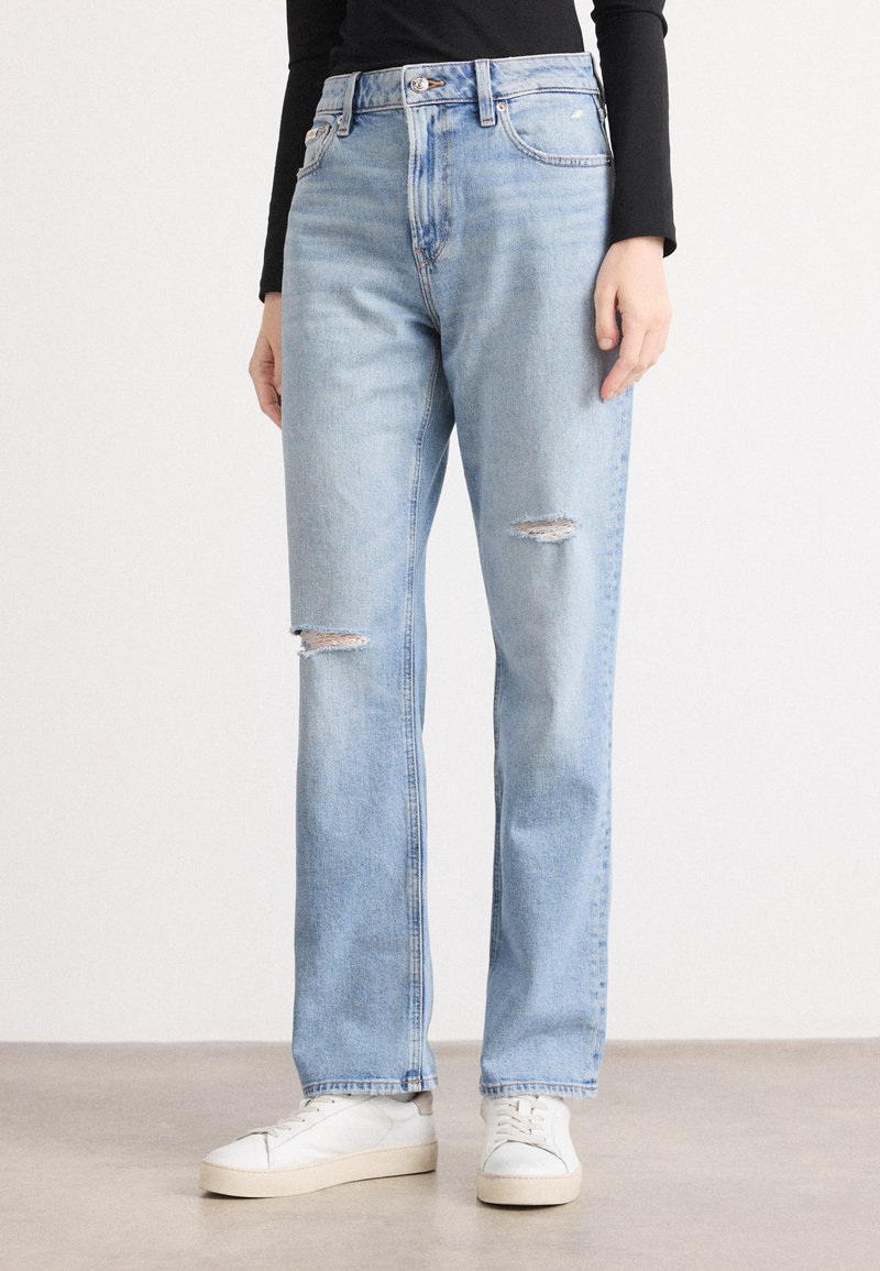 Jeans in denim azzurro chiaro con vita alta, vestibilità dritta e due toppe strappate sul davanti. Abbinati a sneakers bianche.