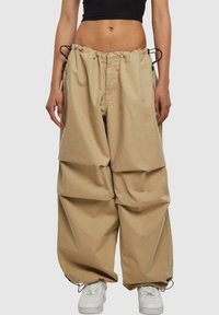 Pantalons larges beiges en tissu léger, dotés d'une taille élastique avec cordons de serrage et de deux poches latérales.