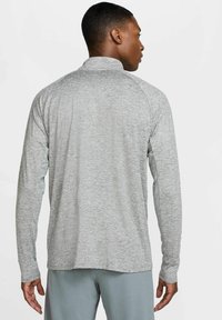 Maglietta atletica a maniche lunghe di colore grigio chiaro, realizzata in tessuto texturizzato. Presenta un colletto e maniche raglan. La vista posteriore mostra una vestibilità rilassata.