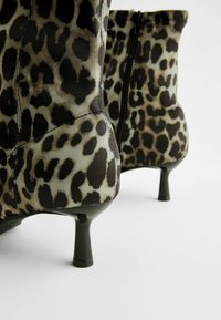 Stivali alla caviglia con stampa leopardata e finitura lucida, dotati di tacchi sottili e neri solidi e di una cerniera laterale per la chiusura.