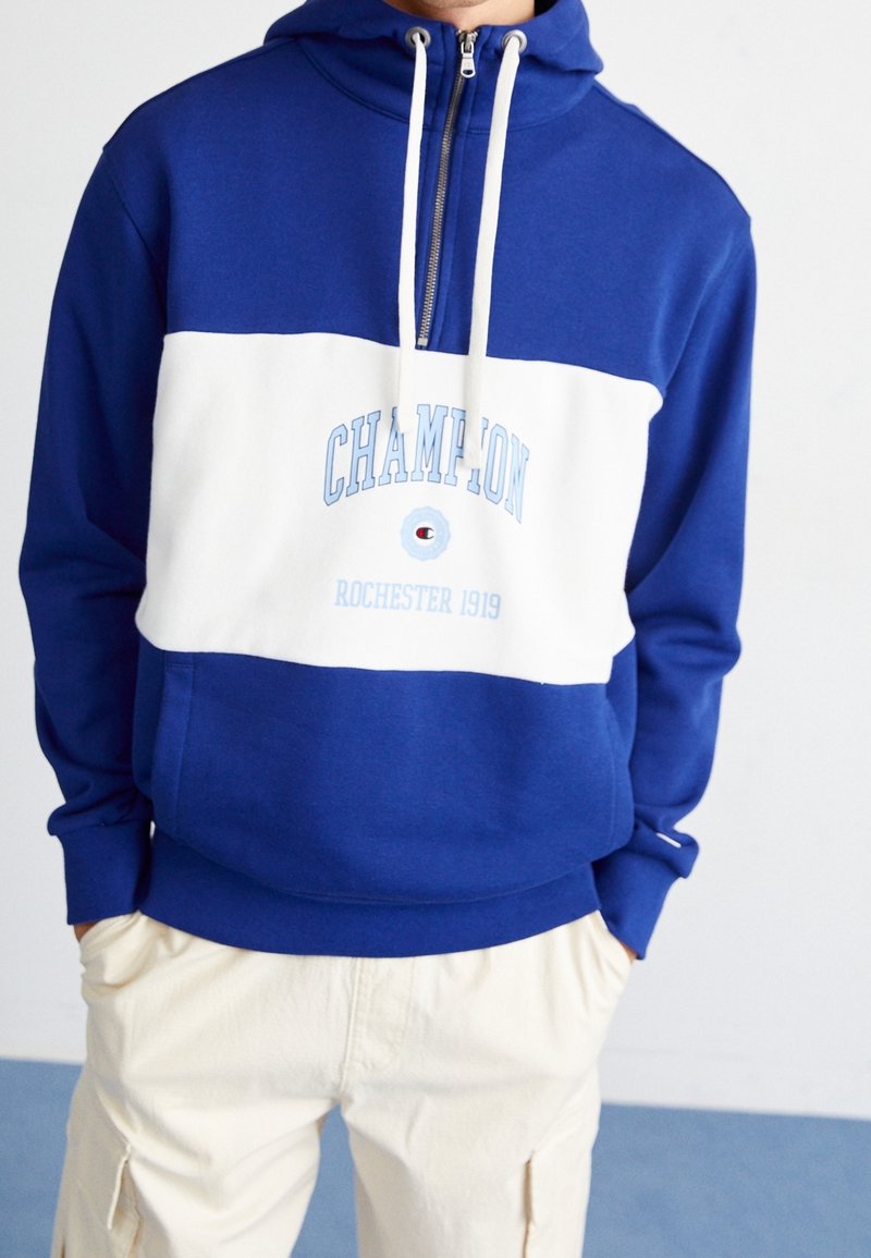 Bluzy z kapturem zapinane na zamek w kolorze niebieskim i białym, z wyraźnym logo, miękkim materiałem, regulowanymi sznurkami oraz teksturowanym wykończeniem.