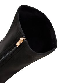 Schwarzer Knöchelstiefel mit glatter Außenseite, ausgestattet mit einem Reißverschluss in Roségold und einem weichen Innenfutter. Entworfen mit einer eleganten, zulaufenden Form.