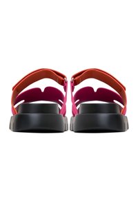 Paire de sandales colorées avec des semelles épaisses noires, des brides roses et rouges, vues de dos sur un fond blanc.