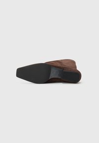 Vue inférieure de bottines en suède marron, présentant une semelle extérieure en caoutchouc noir au texture lisse et un design de bout légèrement pointu.