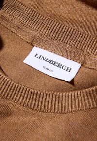 Maglione marrone lavorato a maglia con colletto a girocollo a coste e l'etichetta "LINDBERGH SLIM FIT" visibile su un'etichetta bianca. Texture liscia.