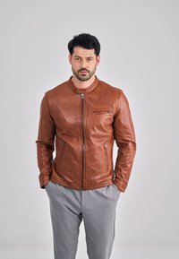Veste en cuir marron au design ajusté, col montant et détails zippés argentés. Comprend deux poches latérales et une poche poitrine.