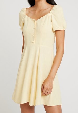 Robe jaune à manches courtes avec un décolleté carré, des boutons sur le devant et une jupe évasée. Fabriquée dans un tissu texturé et léger.