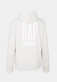 Sweat à capuche gris clair à manches longues, avec un grand texte blanc « GAP EST 1969 » dans le dos.