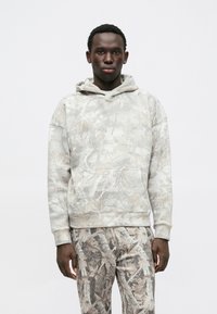 Felpa grigia con un design a motivo foglia, dotata di tasca a marsupio e cappuccio con coulisse, abbinata a pantaloni con motivo coordinato.