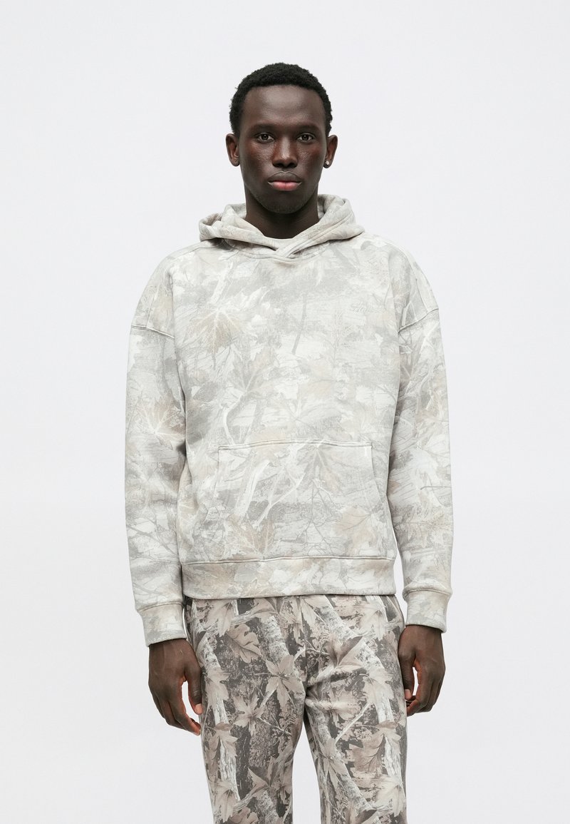 Felpa grigia con un design a motivo foglia, dotata di tasca a marsupio e cappuccio con coulisse, abbinata a pantaloni con motivo coordinato.