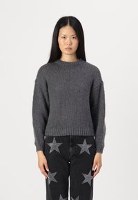 Grå strikkegenser med rund hals og ribbestrikkede mansjetter, kombinert med svarte jeans med sølvstjernes mønster.