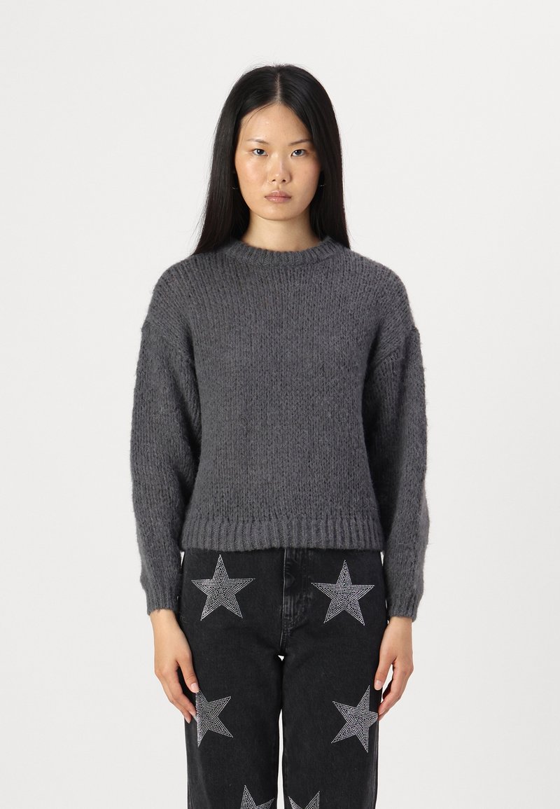 Grå strikkegenser med rund hals og ribbestrikkede mansjetter, kombinert med svarte jeans med sølvstjernes mønster.