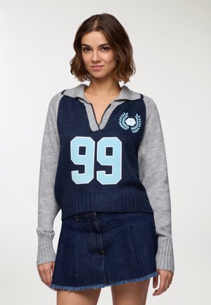 Maglione a maglia blu navy e grigio con collo a polo, caratterizzato dal numero "99" in azzurro chiaro e dettagli con emblema sul petto.
