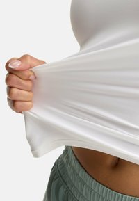 White fitted tank top being pulled, showcasing stretchy fabric and smooth texture. Pairing with loose, mint-green athletic shorts at the waist.