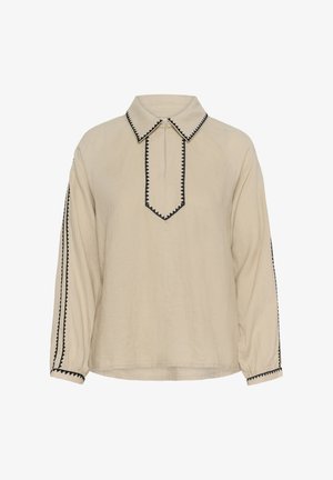 Bézs hosszú ujjú blúz fekete cikk-cakk szegéllyel a galléron, az elülső gombsoron, az ujjsávokon és a mandzsettákon, cipzáras nyakkal.