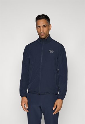 Navy blue lightweight jacket with high collar, zip closure, and EA7 logo. Features long sleeves and elastic cuffs for a fitted look.